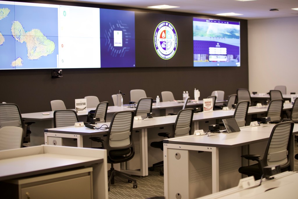 Maui County's brand new emergency command center is equipped with a wall-to-wall video screen of 24 monitors, 24/7 operator workstations, high-tech audio and visual systems, and what one county official called “the dad pad” — a large touch screen where officials can draw on maps, organize ideas and edit plans. (Erin Nolan/Civil Beat/2026)