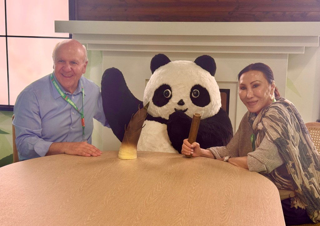 A man and a woman sit at a table with an artificial panda between them