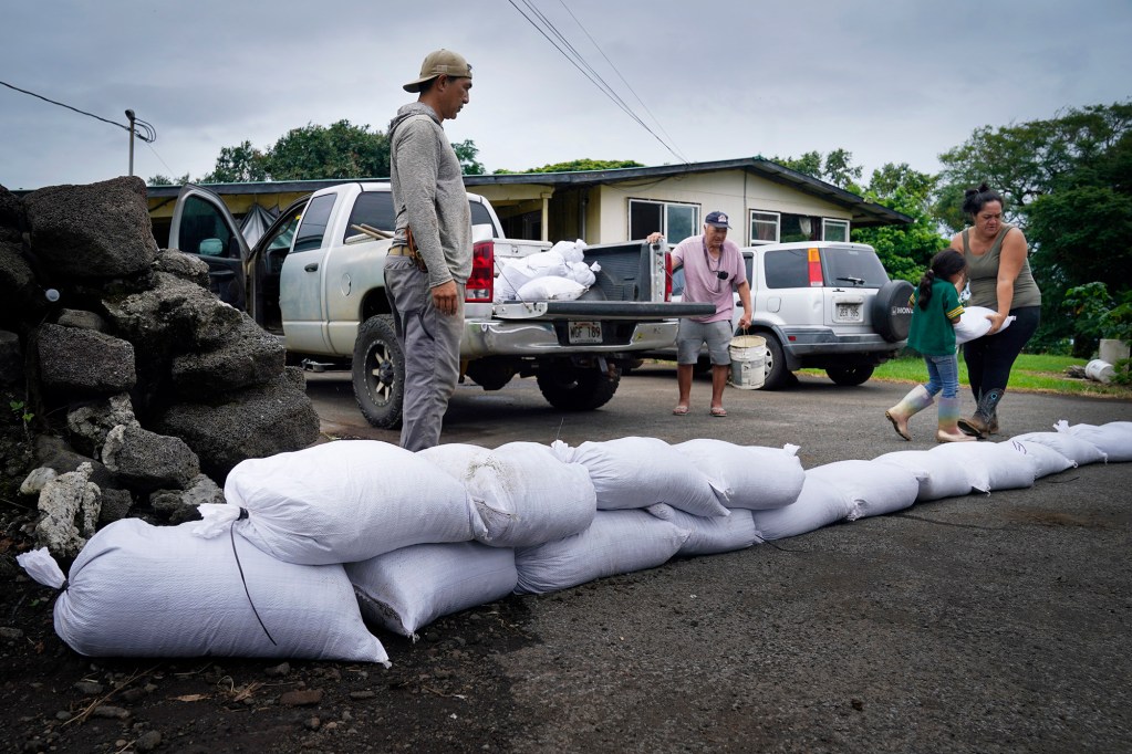 Hanalei Young, from left, and his father Wallace Young watch seven-year-old Sofia Young-Baji  and Alliesen Baji-Young  place a sandbag to block Wallace’s driveway from floodwaters as Hawaiʻi Island prepares for Hurricane Nolo Friday, Sept. 25, 2026, in Waiohinu. Wallace Young’s home flooded during Hurricane Lala. (Kevin Fujii/Civil Beat/2026)