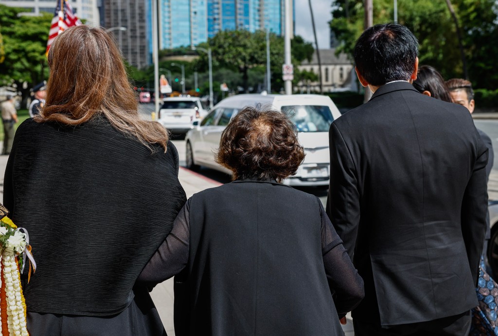 Jean Ariyoshi, middle, widow of former Hawaiʻi Governor George Ariyoshi, watches with daughter-in-law Chika Ariyoshi, left, and son Ryozo Ariyoshi, right, as the hearse carrying the casket of George Ariyoshi arrives at the State Capitol, Friday, Sept. 18, 2026, in Honolulu. Ariyoshi’s casket will lie in state at the State Capitol rotunda through Saturday.  (Jamm Aquino/Civil Beat/2026)
