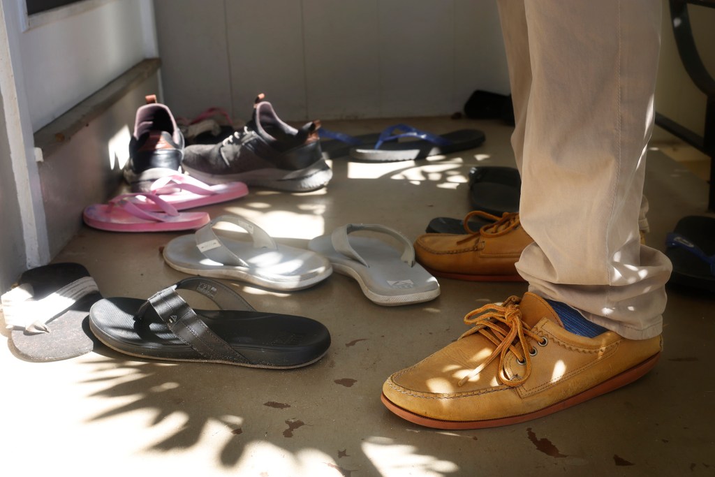 You know you’re campaigning in Hawaiʻi when council candidate Trevor Ozawa has to straddle slippers and shoes outside a Kāhala home Wednesday, Oct. 14, 2026, in Honolulu. (Kevin Fujii/Civil Beat/2026)