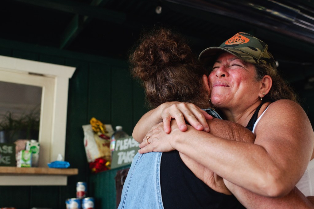 Wainiha, Hi - September 23, 2026: 
Paulina Ann and Joelle Edwards hug each other days after they turned the Wainiha Country Market into a hub for the community after the category 2 Hurricane Lowell caused flooding in Wainiha. In the initial weeks after Lowell, Wainiha Country Market served as a community hub, where residents dropped off empty gas containers. Joell Edwards, who runs the market with her daughter, said other folks would pick those containers up, go fill them up and then return them to the market for residents to pick up. Running on a generator, the market had Starlink Wi-Fi, so it also served as a gathering place where residents could get updates from the county and check in with others elsewhere. The market also had toilet paper, pet food, items for mothers and babies, and a variety of donated food.
Akasha Rabut for The Guardian