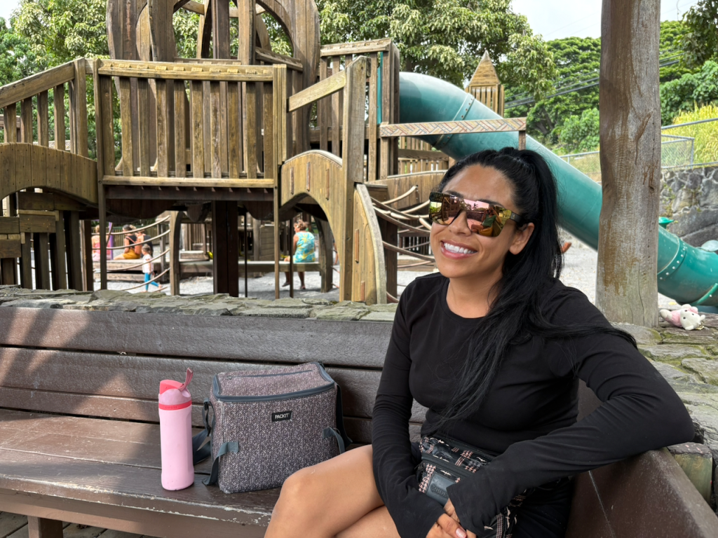 A woman smiles on a bench at a wooden playground 